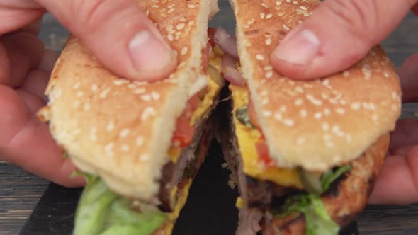 Closeup of the Hands Opening Homemade Burger with Meat Cutlet Cut in Two Halves