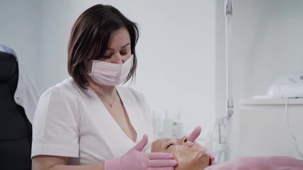 Beautician Puts a Membrane on the Face of a Young Woman with Anesthetic Cream