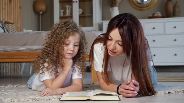 Brunette Mother Reads Book to Little Girl with Curly Hair