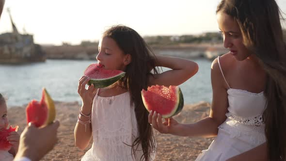Cute Caucasian Girl Eating Watermelon on Family Picnic on Windy Ocean Coast at Golden Sunset