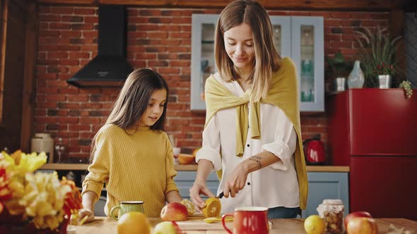 Young Mommy Smiling Cutting Orange for Tea Standing By Table in Kitchen of Country House