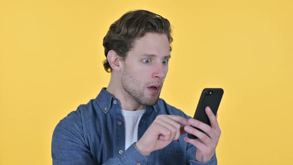 Young Man with Loss on Smartphone Failure on Yellow Background