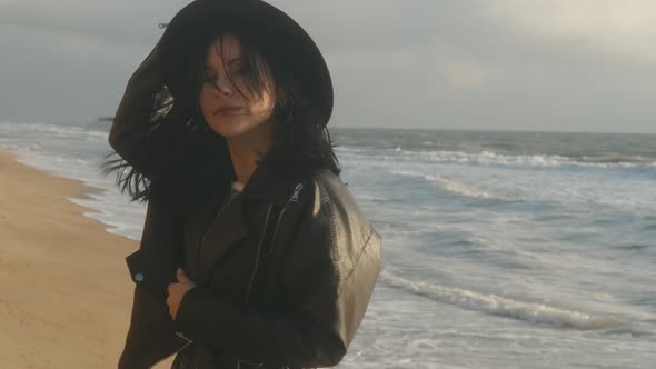 Portrait of Romantic Brunette Woman in Hat and Leather Jacket Walking on the Beach in Autumn at