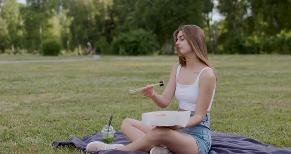 Brunette Woman Filmed From One Side Sitting on a Blanket in the Park and Eating Sushi with