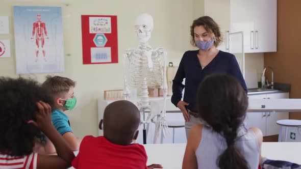 Female teacher wearing face mask using human skeleton model to teach students in class