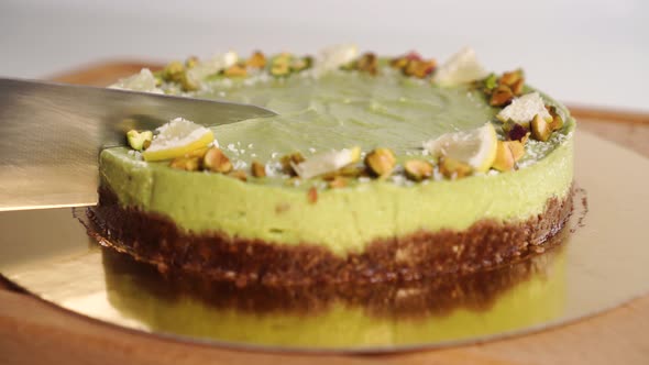 A hand with a kitchen knife slices an organic homemade avocado cake