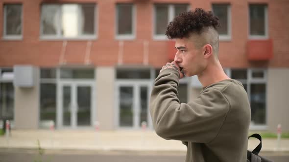 A young man walks through the city and blows smoke from an electronic cigarette