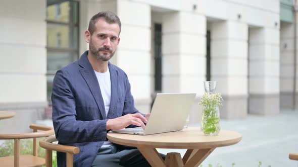 Man Showing Thumbs Down While Using Laptop Sitting in Outdoor Cafe