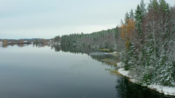 Swedish lake AERIAL shot, flying along the lakeside forest, glassy water