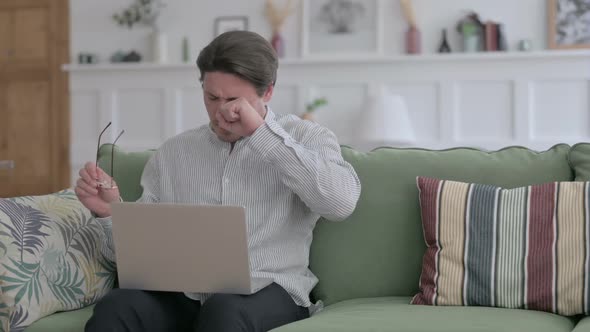 Young Man with Laptop having Headache on Sofa