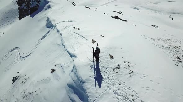 Aerial drone circling view of a skier with skis on top of a snow covered mountains in the winter.