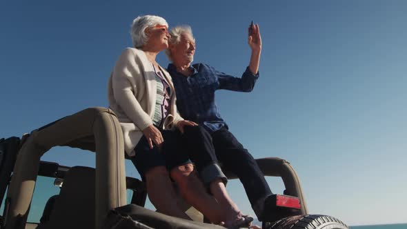 Senior couple taking photos sitting on a car