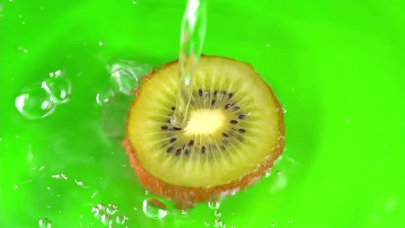 Water pours on green hue juicy kiwi fruit on green background slow motion closeup. Kiwi fruit