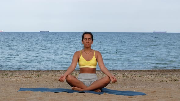 Beautiful tanned young woman sitting in a meditation pose on the beach. Goods for health.