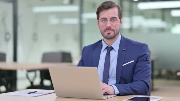 Serious Young Businessman with Laptop Looking at Camera