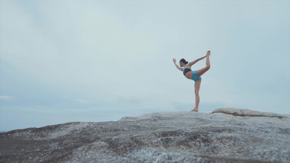 Woman Standing on One Leg and Meditating on Rocks Near Ocean