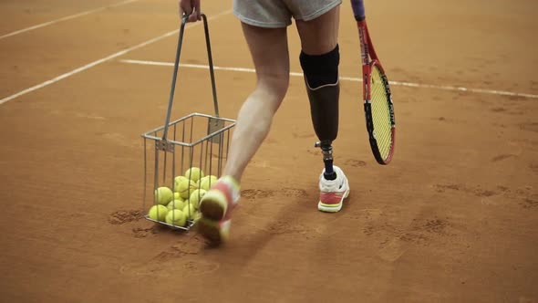 Tracking Footage of a Sports Girl with a Prosthesis on Her Right Foot Picking Up Tennis Balls with