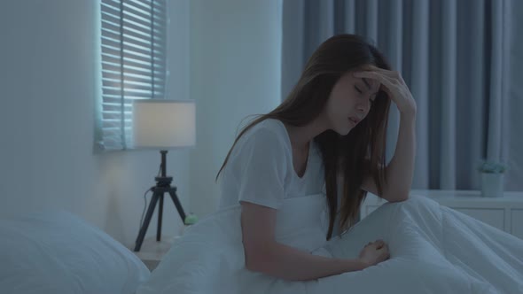 Asian beautiful upset depressed girl sitting alone on bed in dark night room at home.