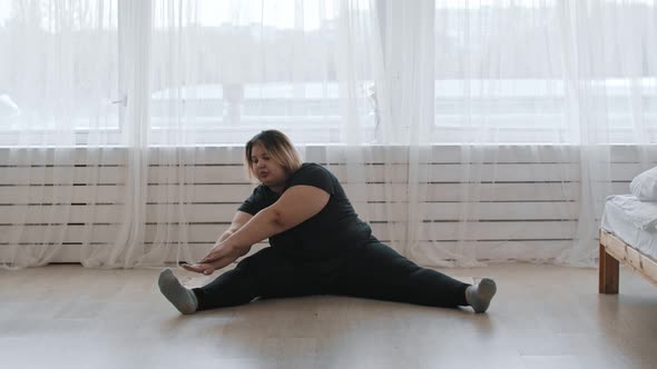 A Fat Woman Sitting on the Floor and Doing Stretching Exercises