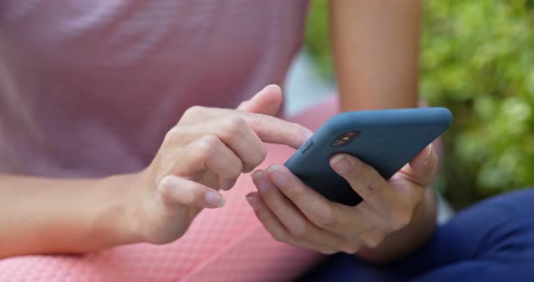 Woman use of mobile phone with her yoga mat at outdoor