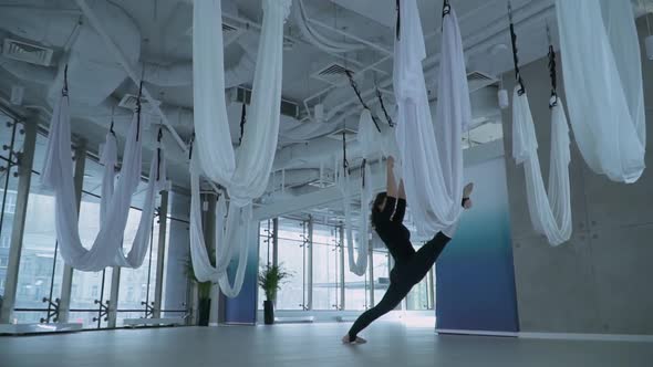 Beautiful Woman Doing Leg Stretching Puts One Leg in Hammock for Yoga and Another on the Floor in