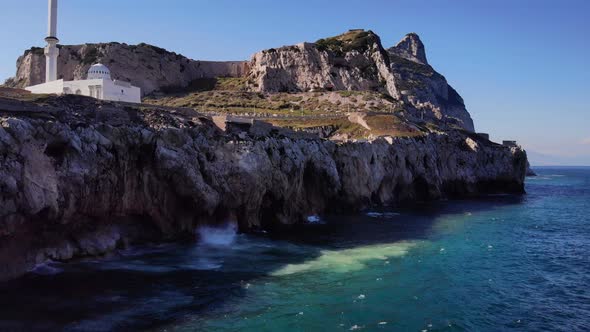 Sea Waves Hitting The Rocky Europa Point Of Gibraltar With View Of Ibrahim-al-Ibrahim Mosque And The