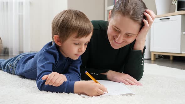 Smiling Boy Lying on Floor and Doing Homework with His Mother