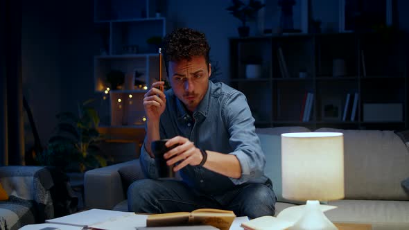 Young Man Drinking Coffee While Studying at Home in the Evening