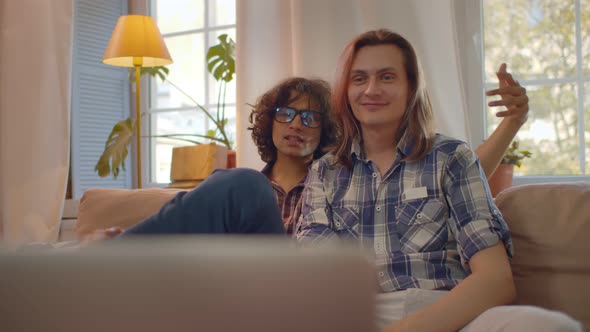 Homosexual Male Couple at Home on Couch Working and Communicating Via Laptop