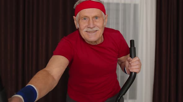 Healthy Elderly Senior Grandfather Model Exercising Sport Workout on Orbitrek in Room at Home