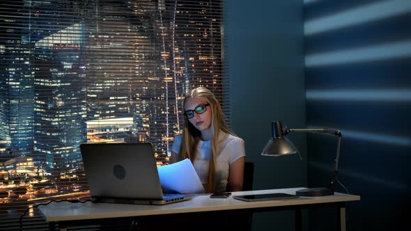 Young Female Professor Correcting Her Report Late at Night and Checking Smartphone