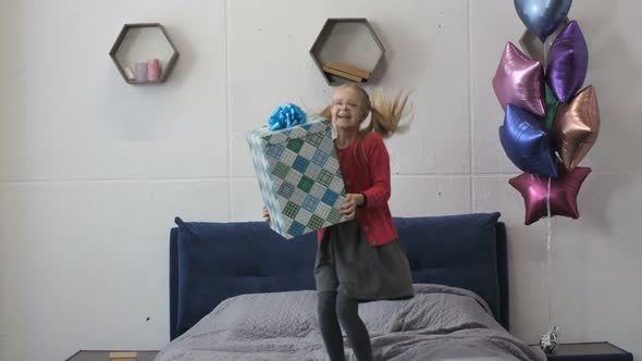 Happy Girl Jumping on Bed with Big Gift Box