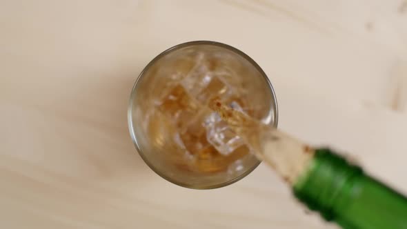 Top View Cold Rum or Whiskey Drink Pouring From Green Bottle in Glass With Ice Cubes Wooden Table