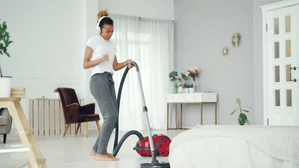 Creative African American Teenager Is Hoovering Floor in Nice Apartment, Listening To Music with
