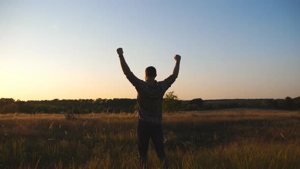 Happy Guy Going Through Grass Field and Victoriously Raising Hands Up at Sunset