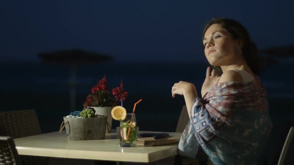 Flirty Young Lady Touching Hair, Enjoying Rest at Outdoor Seaside Restaurant