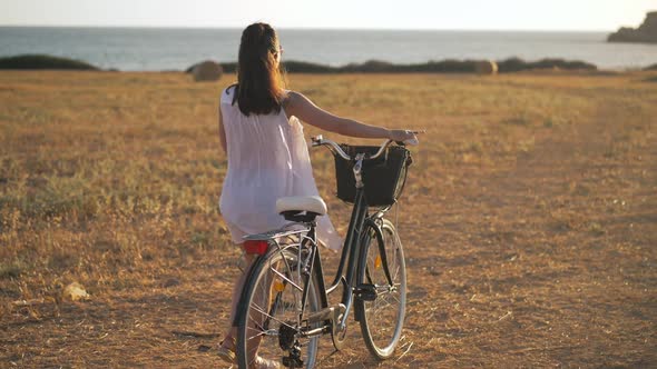 Wide Shot Happy Young Woman Walking with Bike at Sunset on Yellow Farm on Cyprus Looking Back in
