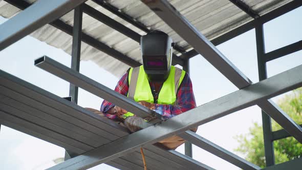 Asian male welder is welding steel beams in process of home renovation for building construction.