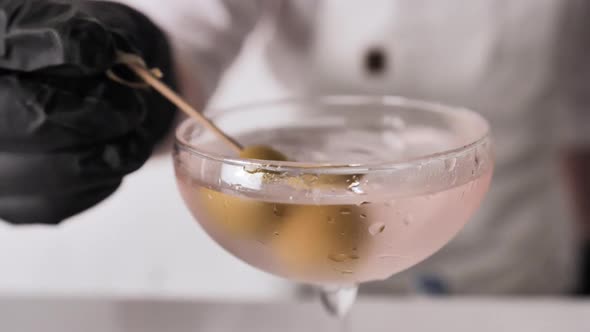 Bartender Puts Olives into Martini Cocktail Glass Close Up