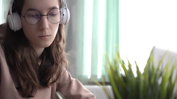 A Girl Takes Notes in a Notebook From Her Laptop