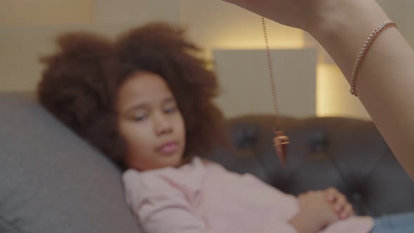 Closeup of Psychotherapist Hand Hypnotizing Lovely Black Kid Using Pendulum