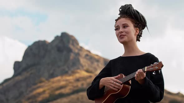 Young Woman with Dreadlocks Playing Ukulele in Mountains