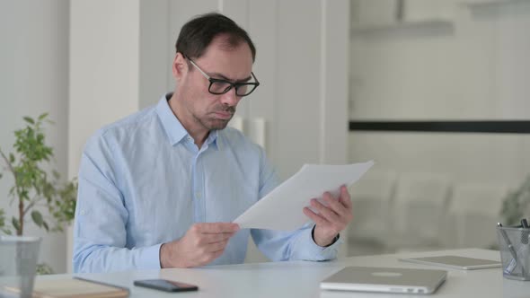 Middle Aged Man Reading Documents in Office