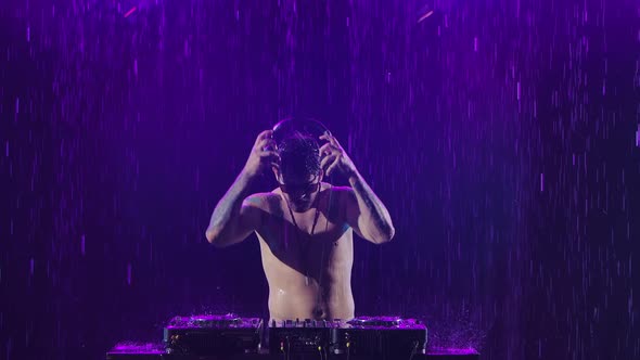 A Sexy Male Dj with a Shiny Body From the Rain Plays on the Remote Control for Mixing Music in a