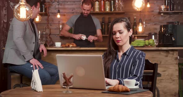 Young Woman in a Coffee Shop Laughs While Composing a Text on Her Notebook