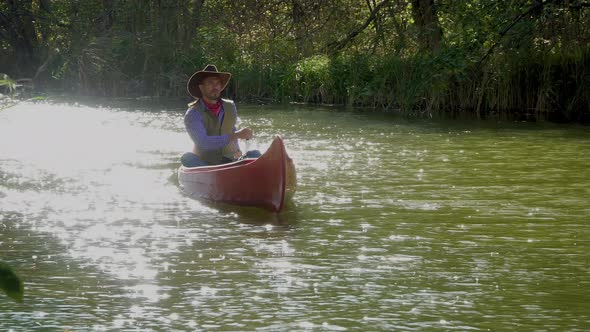 Cowboy in a Canoe Floats on the River in the Forest