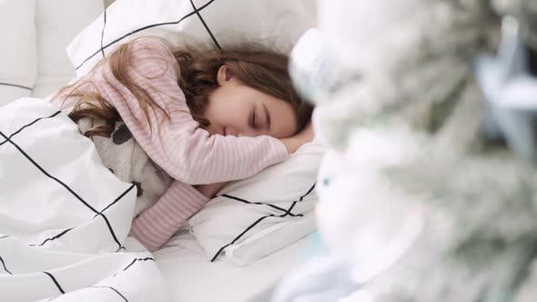 Little Girl Sleeps on the Background of the Christmas Tree. Girl Sleeping on Bed at Christmas