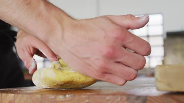 Caucasian male chef kneading dough on a kitchen table