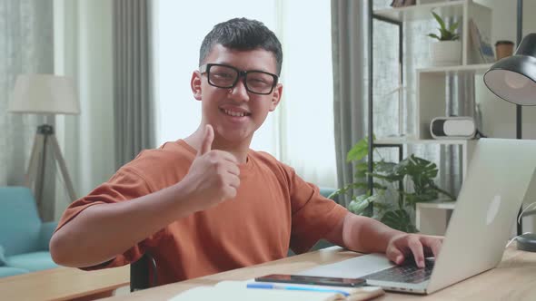 Young Asian Boy Sitting In A Wheelchair Using Laptop Computer While Smiling And Thumb Up To Camera
