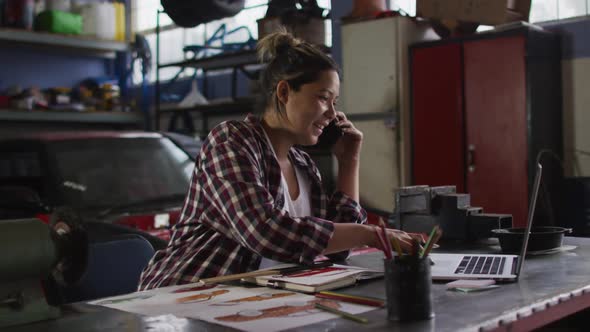 Female mechanic talking on smartphone and using laptop at a car service station